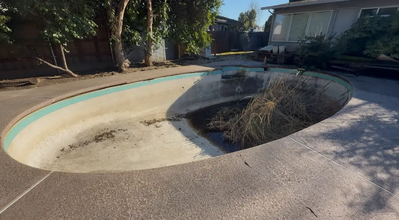 Abandoned in-ground kidney pool with debris and overgrowth in Sacramento backyard