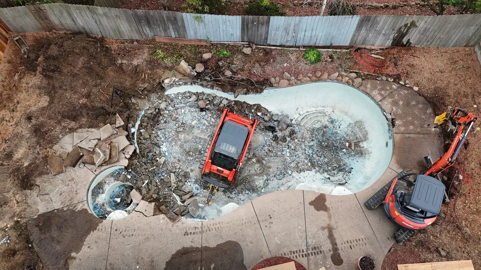 Aerial view of a Demo Patrol pool demolition in a Sacramento backyard with Kubota excavator breaking out the concrete shell